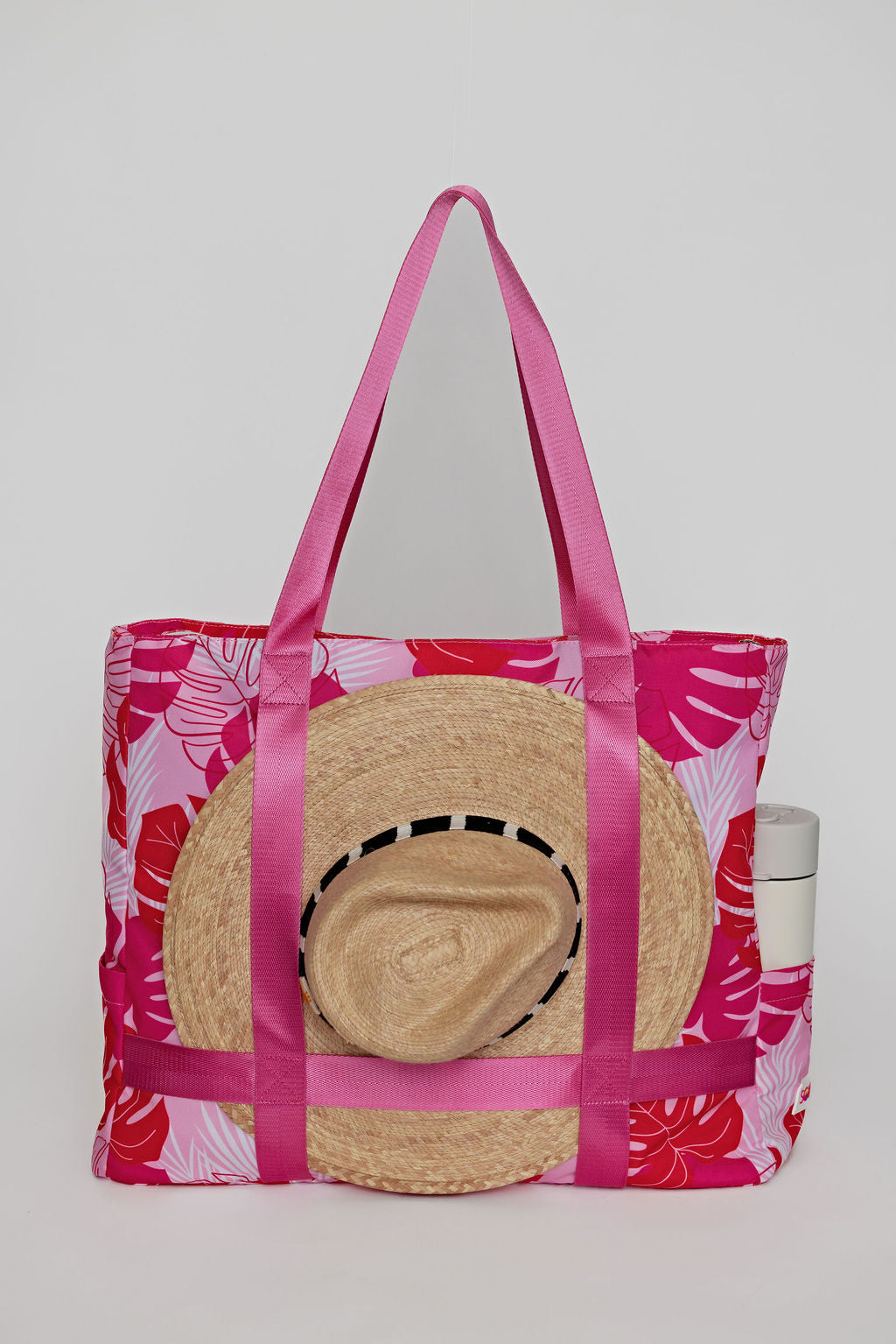 Pink tote bag with floral pattern and straw hat on a white background